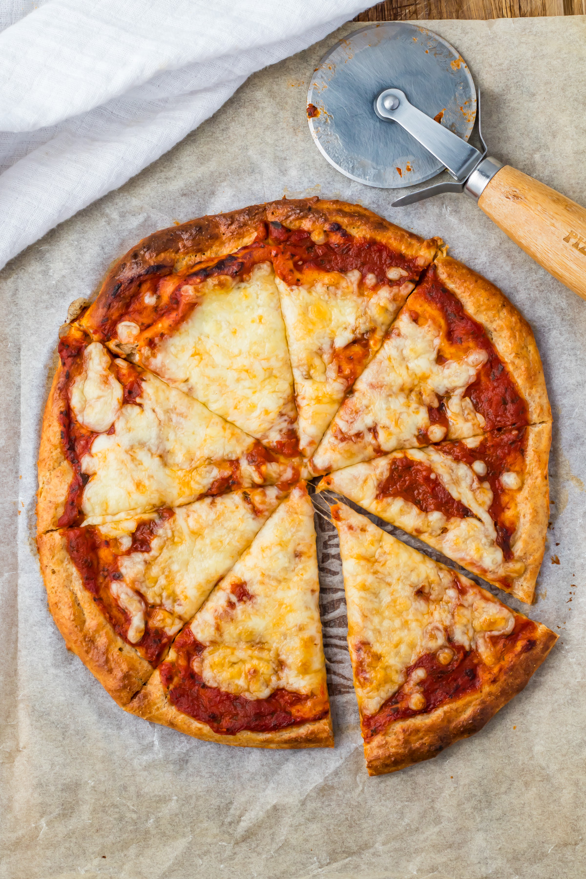 Sliced cottage cheese pizza on parchment paper with a pizza cutter placed beside it.