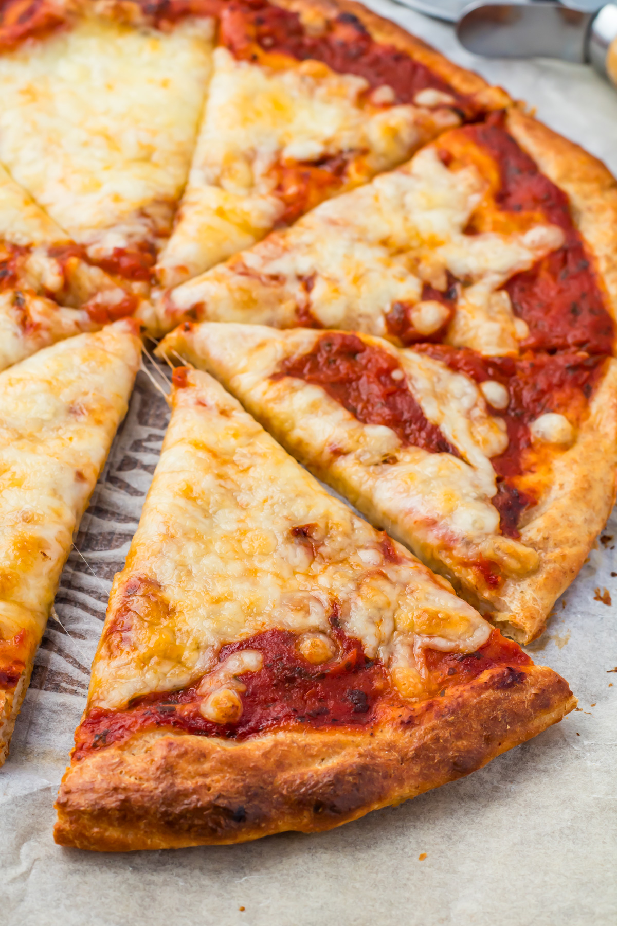 A close-up of a sliced cottage cheese pizza with melted cheese and tomato sauce on a parchment-lined surface.