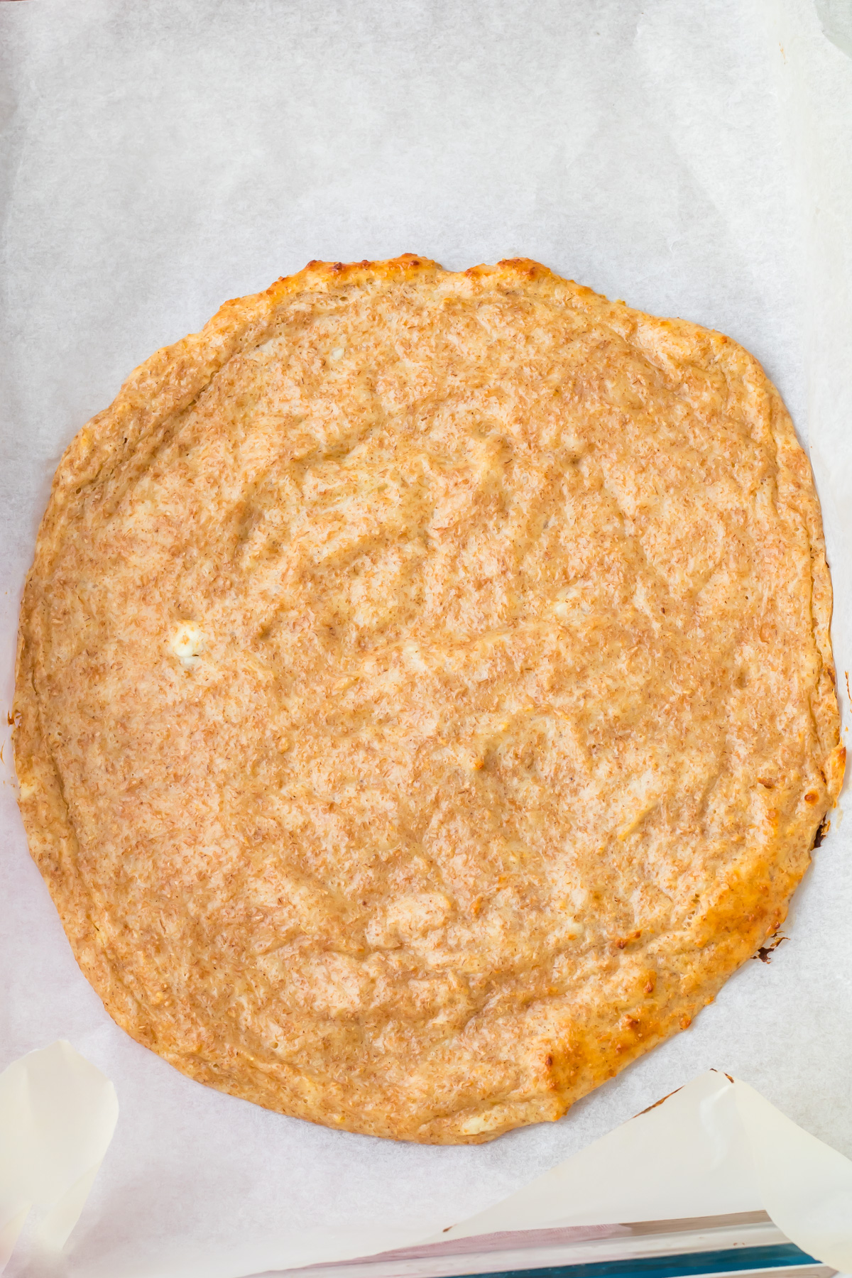 A round, baked cottage cheese pizza crust sits on a sheet of parchment paper.
