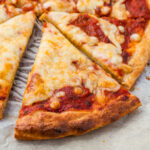 A close-up of cottage cheese pizza slices on parchment paper, showing melted cheese, tomato sauce, and a golden-brown crust.
