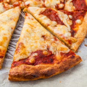 A close-up of cottage cheese pizza slices on parchment paper, showing melted cheese, tomato sauce, and a golden-brown crust.