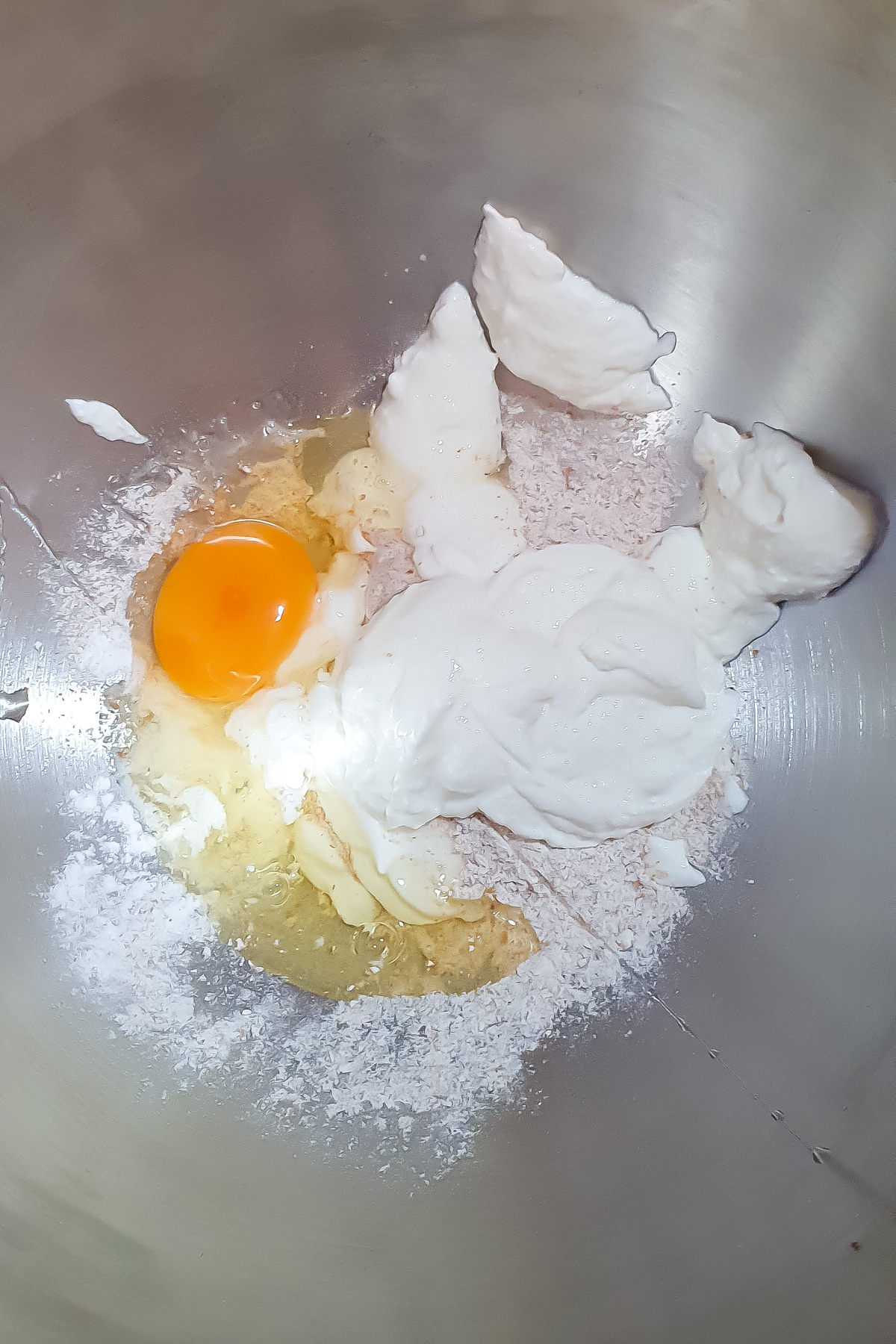 A close-up of a mixing bowl containing an egg, flour, cottage cheese, and other baking ingredients.