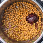 Cooked instant pot chickpeas with a whole red onion, surrounded by cooking liquid.