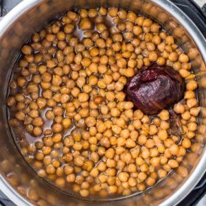 Cooked instant pot chickpeas with a whole red onion, surrounded by cooking liquid.