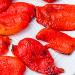 Several pieces of roasted red peppers are arranged on a white plate.