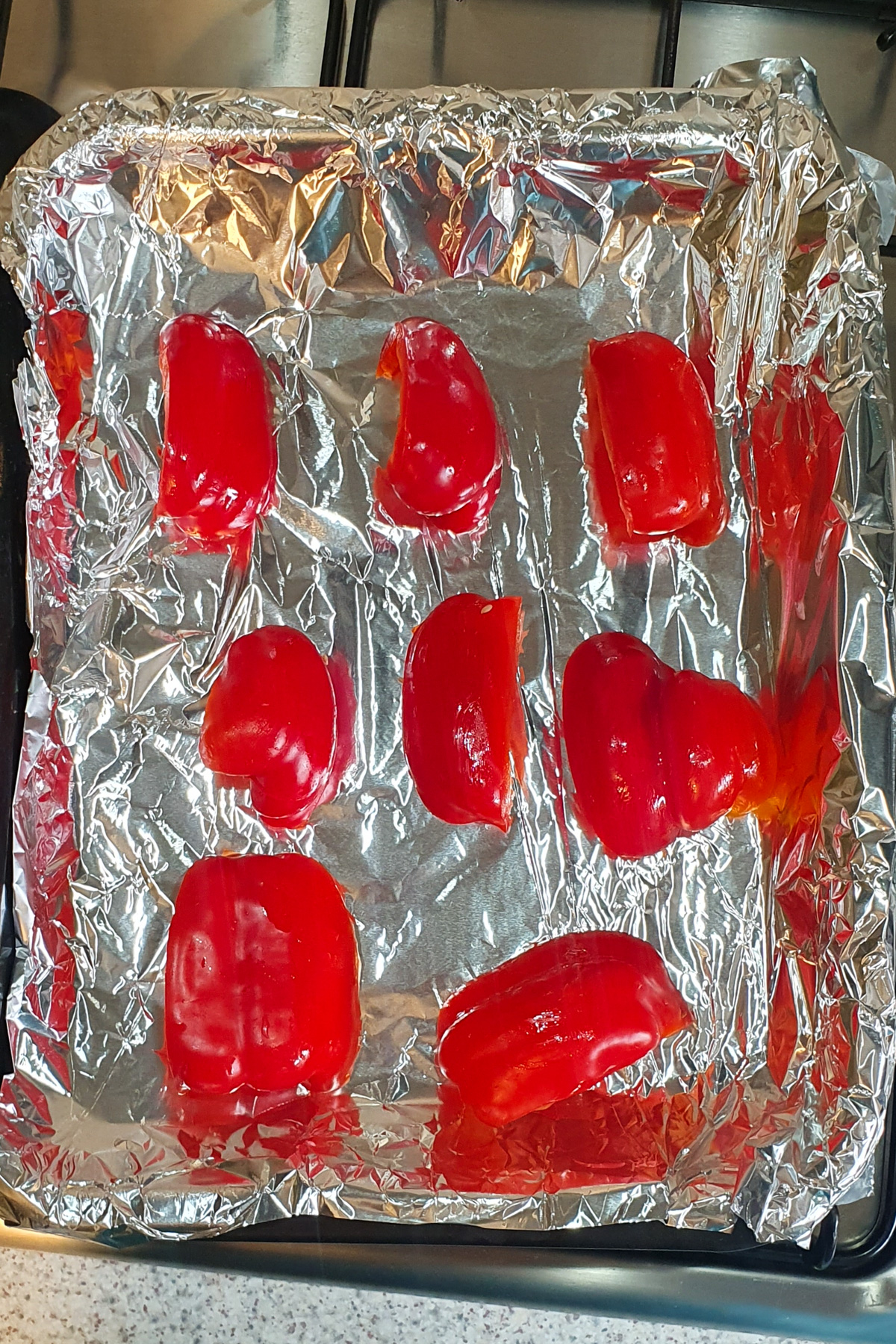 Nine red bell pepper pieces are arranged on a foil-lined baking tray, ready for roasting.