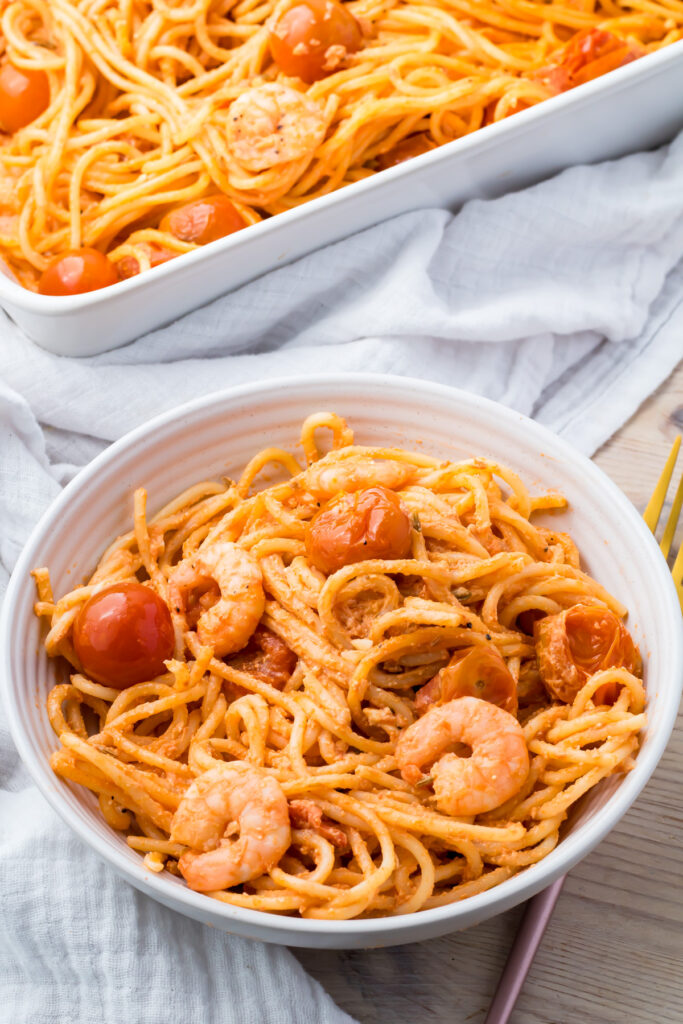 A bowl of shrimp feta pasta with a baking dish of the same pasta in the background.