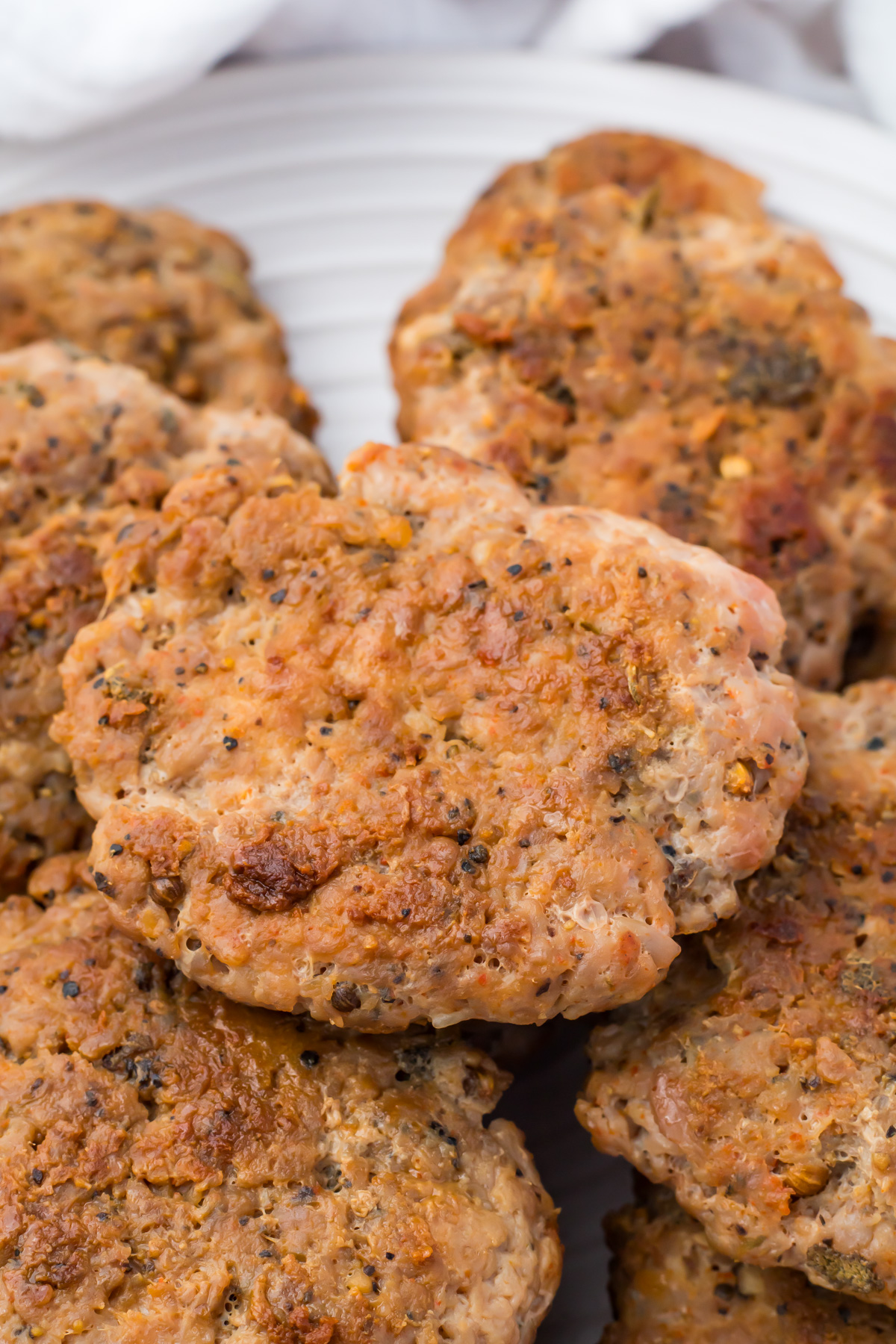 Several browned turkey sausage patties stacked on a white plate, showing a coarse texture with visible spices.