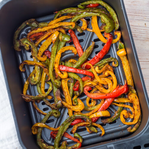 Sliced red, yellow, and green bell peppers cooked in an air fryer basket, seasoned and slightly charred.