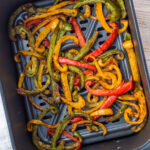 Sliced red, yellow, and green bell peppers cooked in an air fryer basket, lightly browned and seasoned.