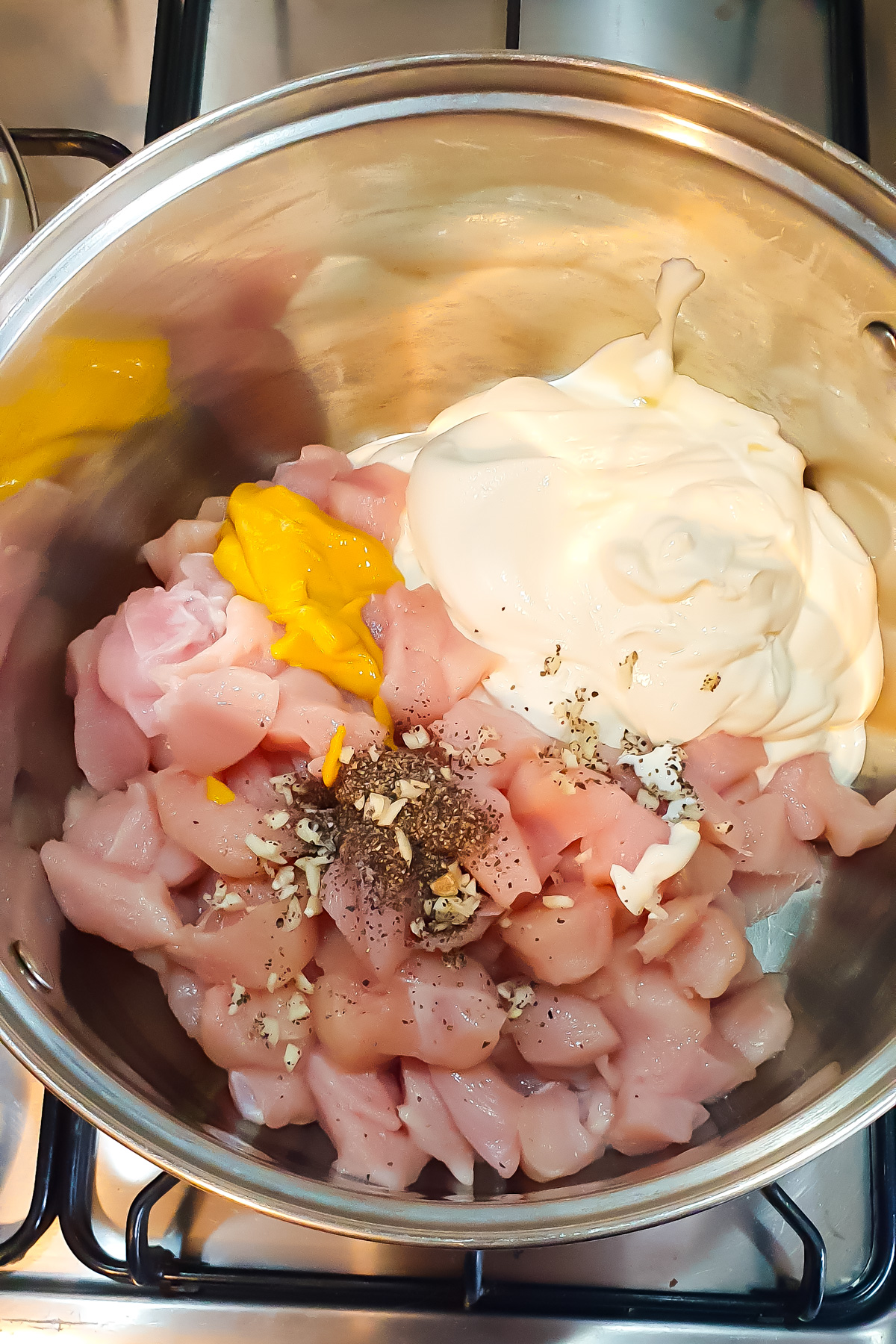 A pot on a stove containing raw diced chicken, Greek yogurt, mustard, minced garlic, and black pepper.