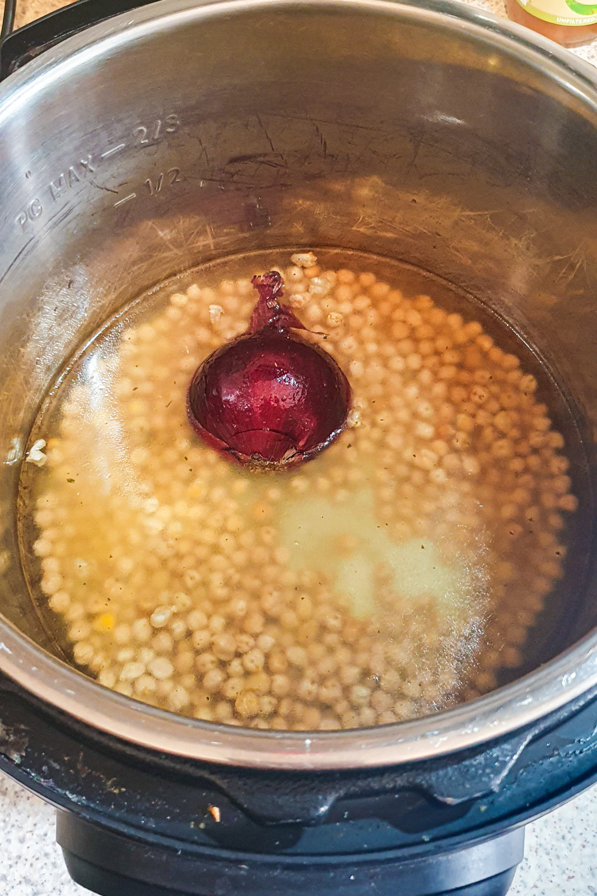 Chickpeas and a halved red onion in water inside a stainless steel Instant Pot on a kitchen countertop.