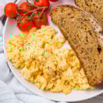 A plate with scrambled eggs (without milk) topped with black pepper, two slices of whole grain toast, and a cluster of vine tomatoes.