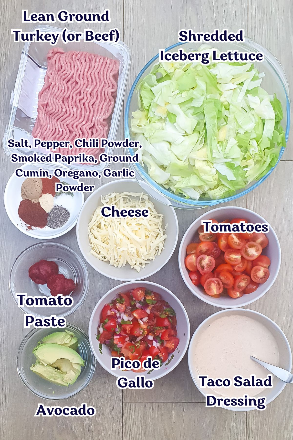 Various taco salad ingredients are arranged in bowls: ground turkey or beef, shredded lettuce, shredded cheese, tomato paste, sliced tomatoes, pico de gallo, avocado, and taco salad dressing.