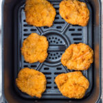 Five breaded ground chicken nuggets arranged inside an air fryer basket, ready for cooking.