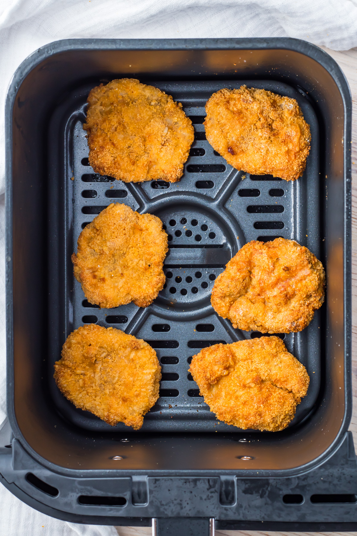 Five breaded ground chicken nuggets arranged inside an air fryer basket, ready for cooking.