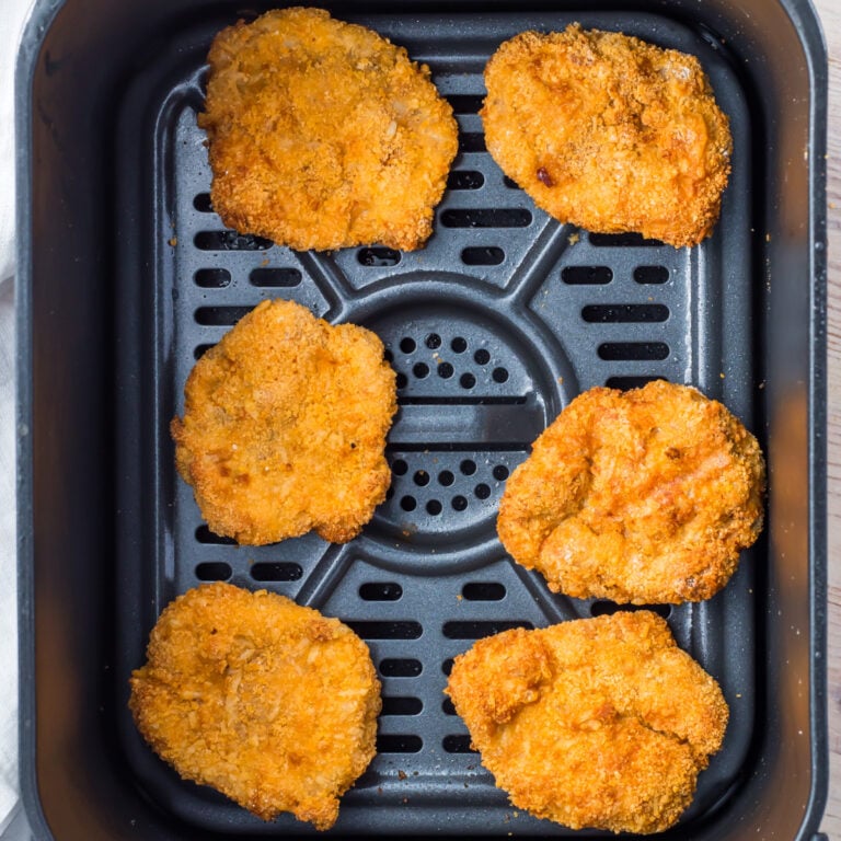 Six breaded ground chicken nuggets arranged in an air fryer basket.