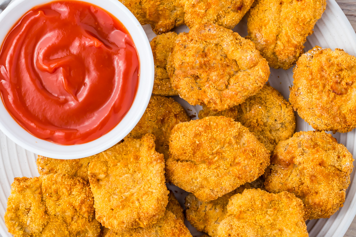 A plate of golden brown air fryer chicken nuggets arranged around a small bowl of red ketchup.