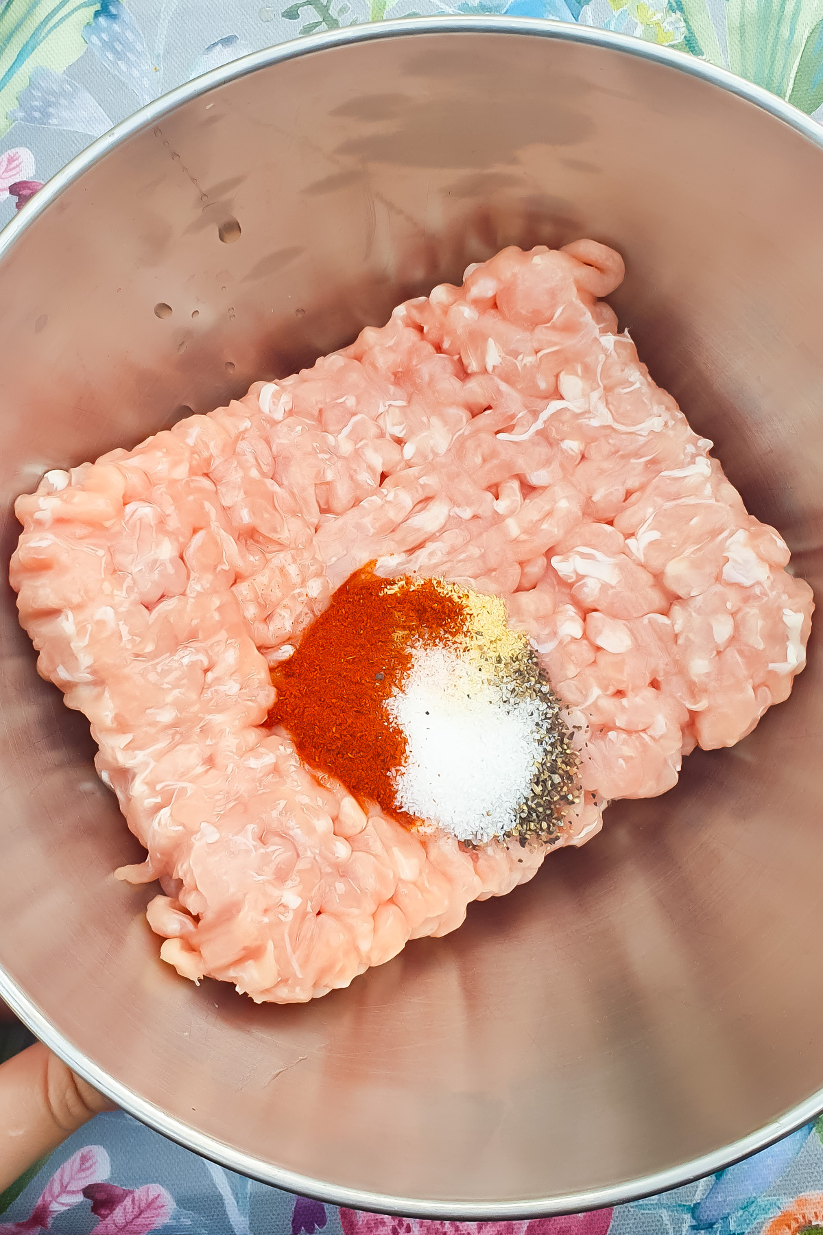 Ground chicken in a metal bowl with piles of paprika, salt, black pepper, onion powder, and garlic powder on top.