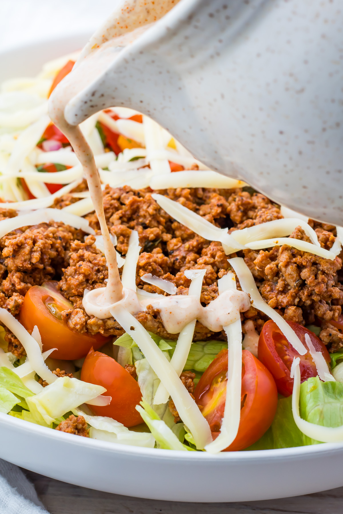 Taco salad is topped with creamy Mexican Salad dressing being poured from a white pitcher.