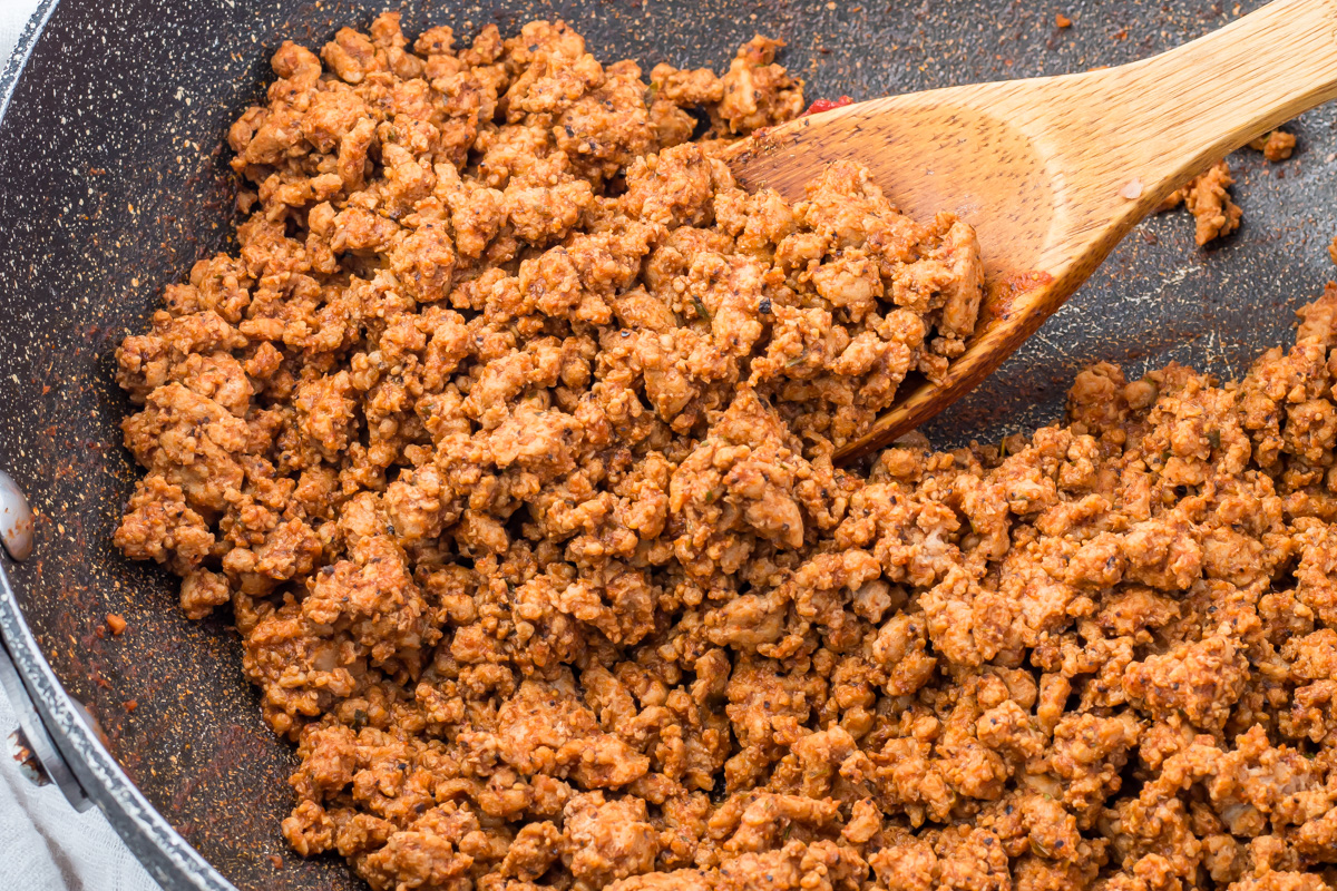 Cooked Mexican taco meat with spices in a pan, being stirred with a wooden spoon.