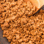 Cooked Mexican taco meat with seasoning in a skillet, being stirred with a wooden spoon.