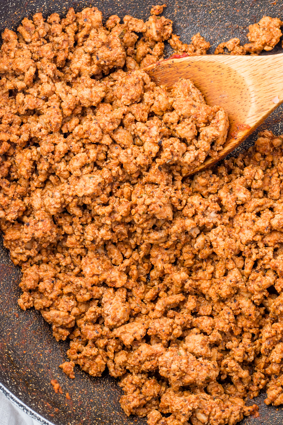Cooked Mexican taco meat with seasoning in a skillet, being stirred with a wooden spoon.