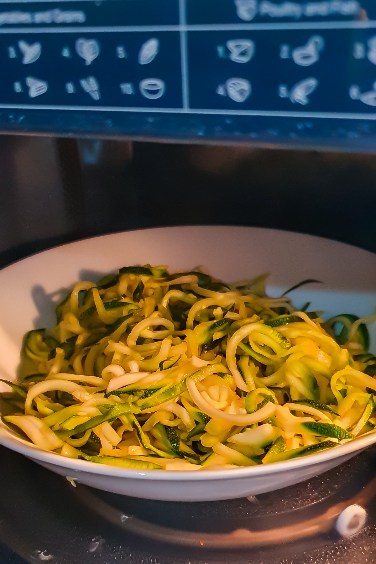 A bowl of zucchini noodles sits inside a microwave, ready to be heated.