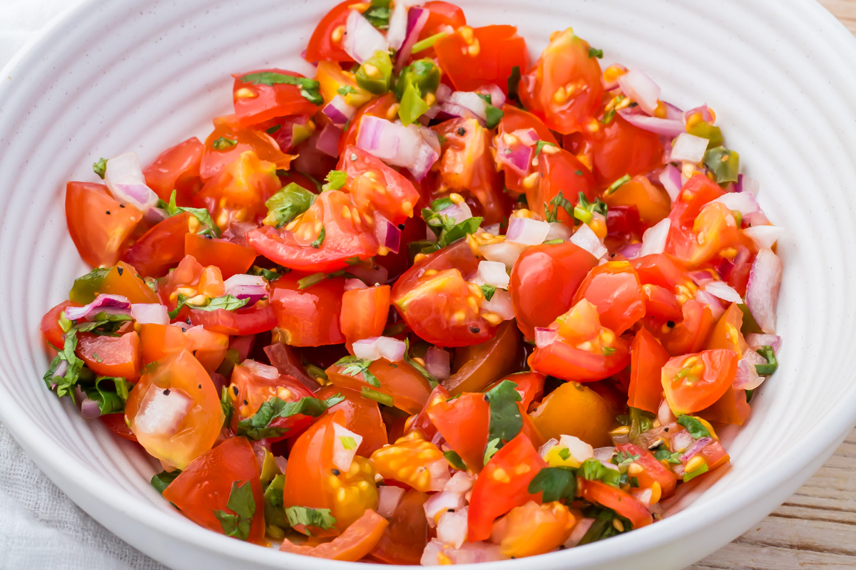 A white bowl filled with chopped tomatoes, red onions, cilantro, and green peppers, resembling a fresh taco salsa.
