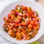 A white bowl filled with chopped cherry tomatoes, red onions, cilantro, and green peppers, resembling a fresh taco salsa.