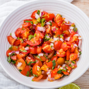 A white bowl filled with chopped cherry tomatoes, red onions, cilantro, and green peppers, resembling a fresh taco salsa.