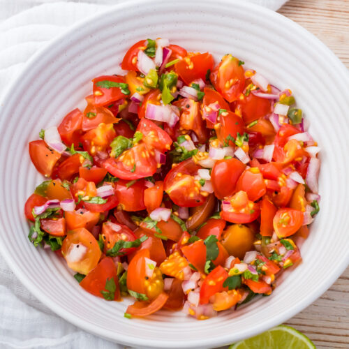 A white bowl filled with chopped cherry tomatoes, red onions, cilantro, and green peppers, resembling a fresh taco salsa.