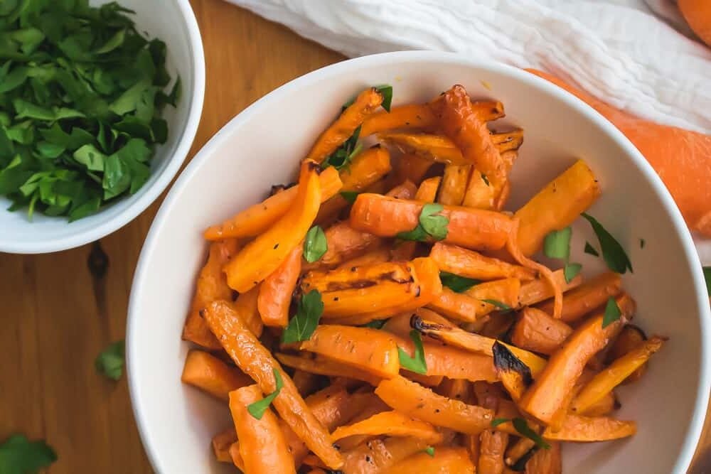 overhead shot of bowl of air fryer carrots next to bowl of parsley