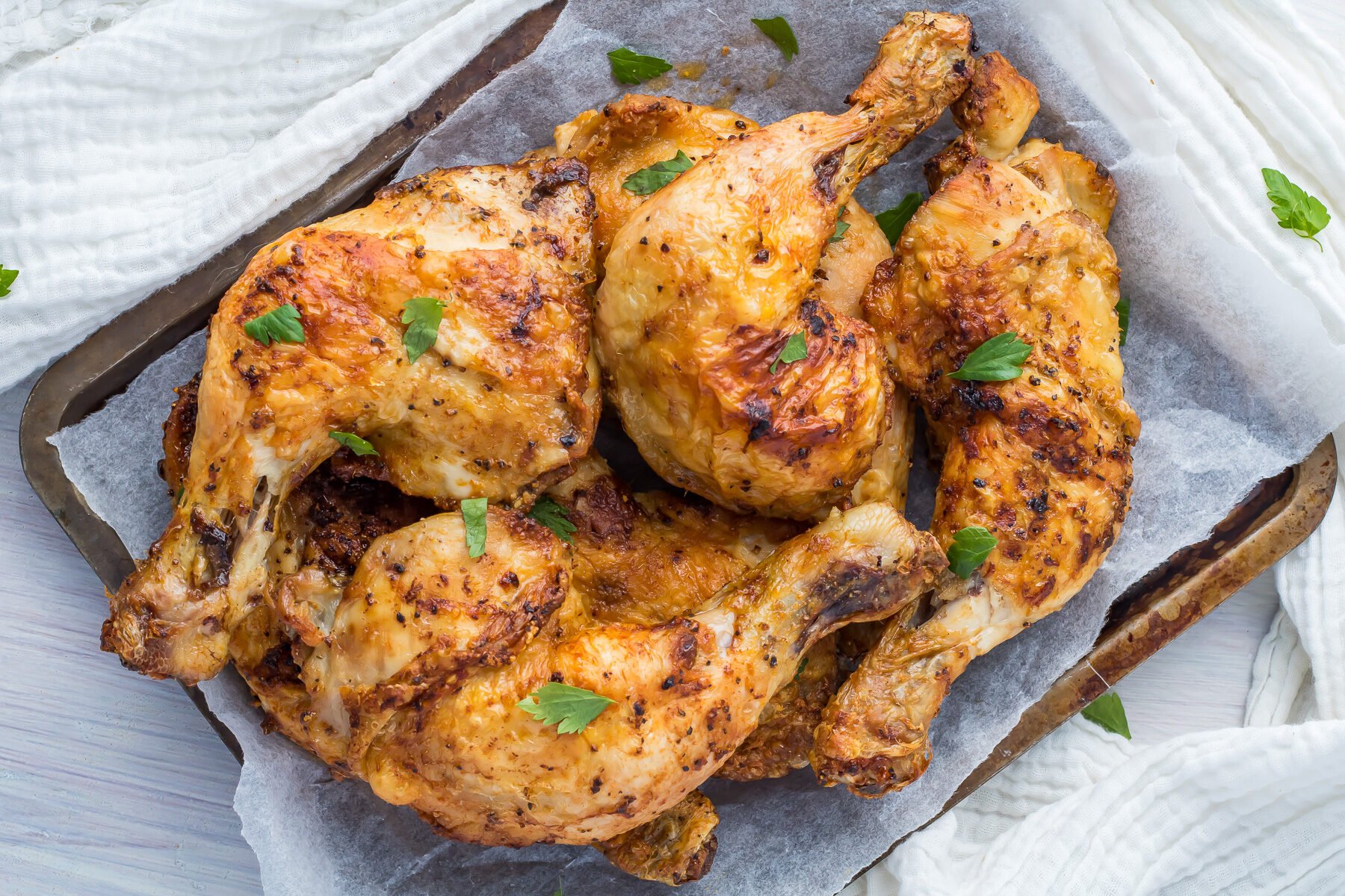 Air Fryer Chicken legs on a metal tray with parchment paper next to a white cloth.