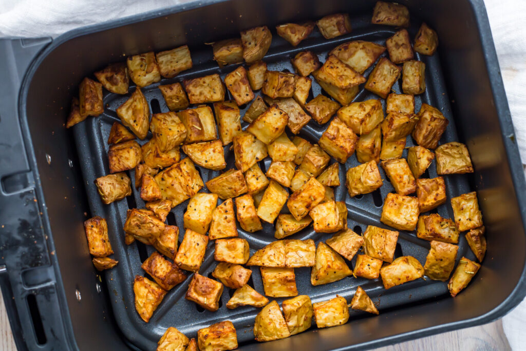 Seasoned diced potatoes are evenly spread inside an air fryer basket, appearing golden brown and roasted.