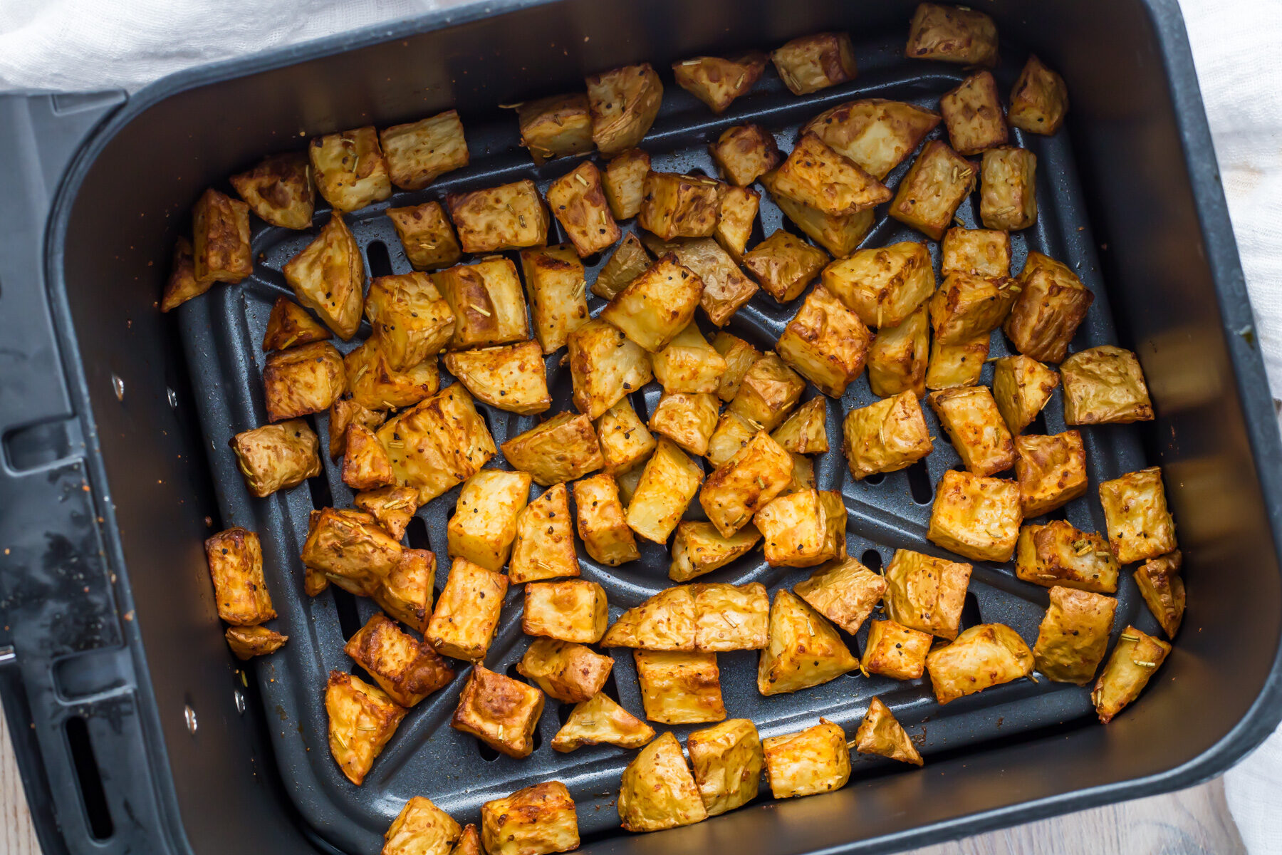 Seasoned diced potatoes are evenly spread inside an air fryer basket, appearing golden brown and roasted.