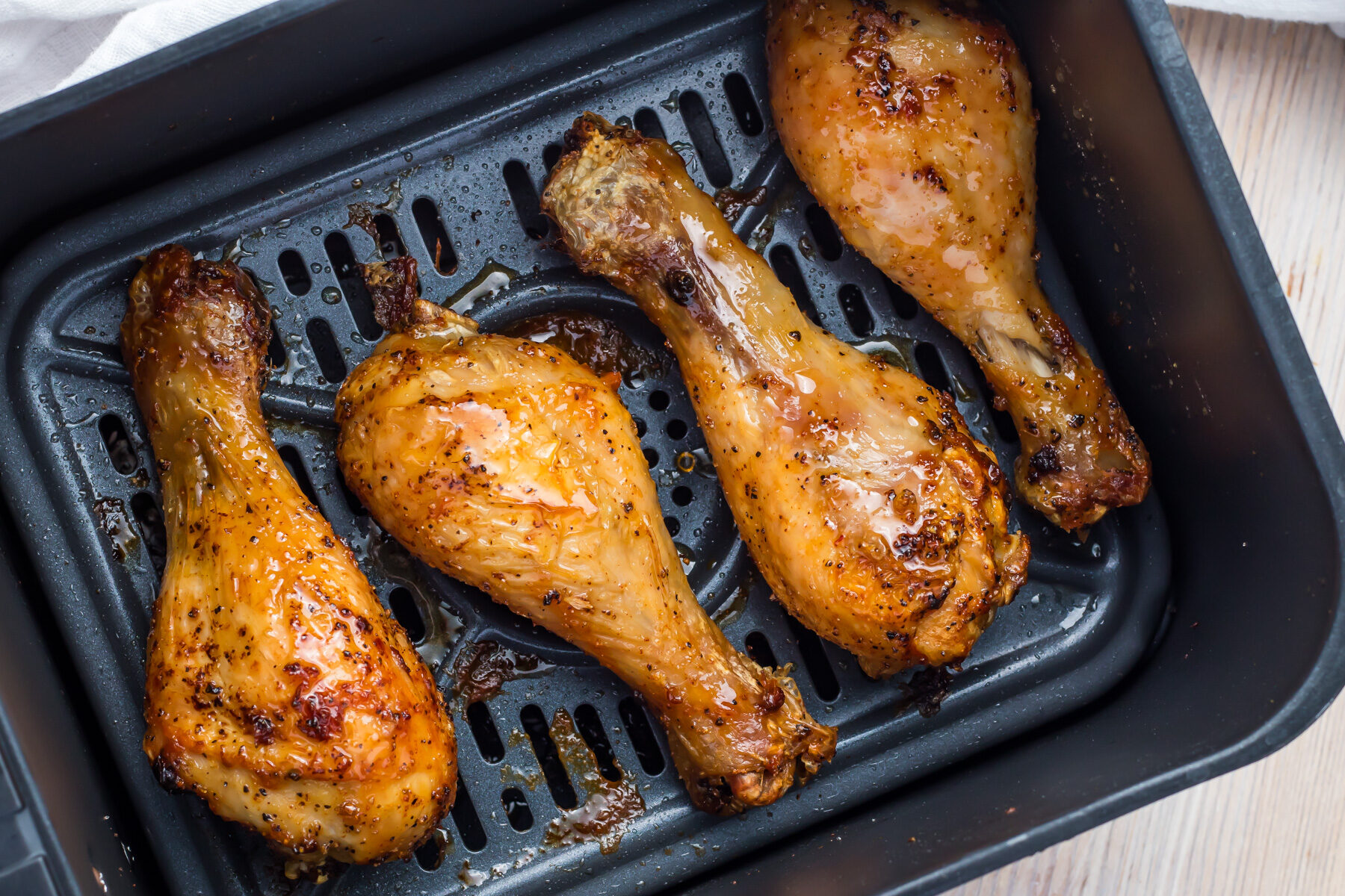 Close-up of three air fryer hot honey chicken drumsticks in an air fryer basket.