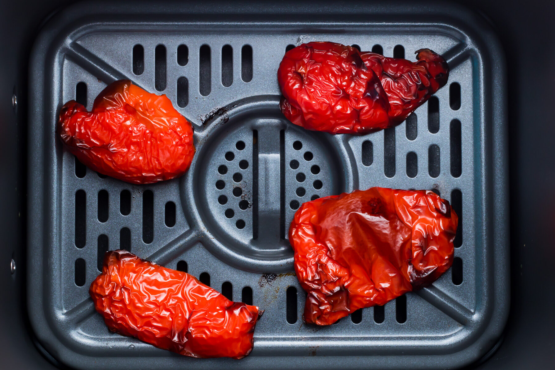 Four air fryer roasted red bell pepper halves on the tray of an air fryer.