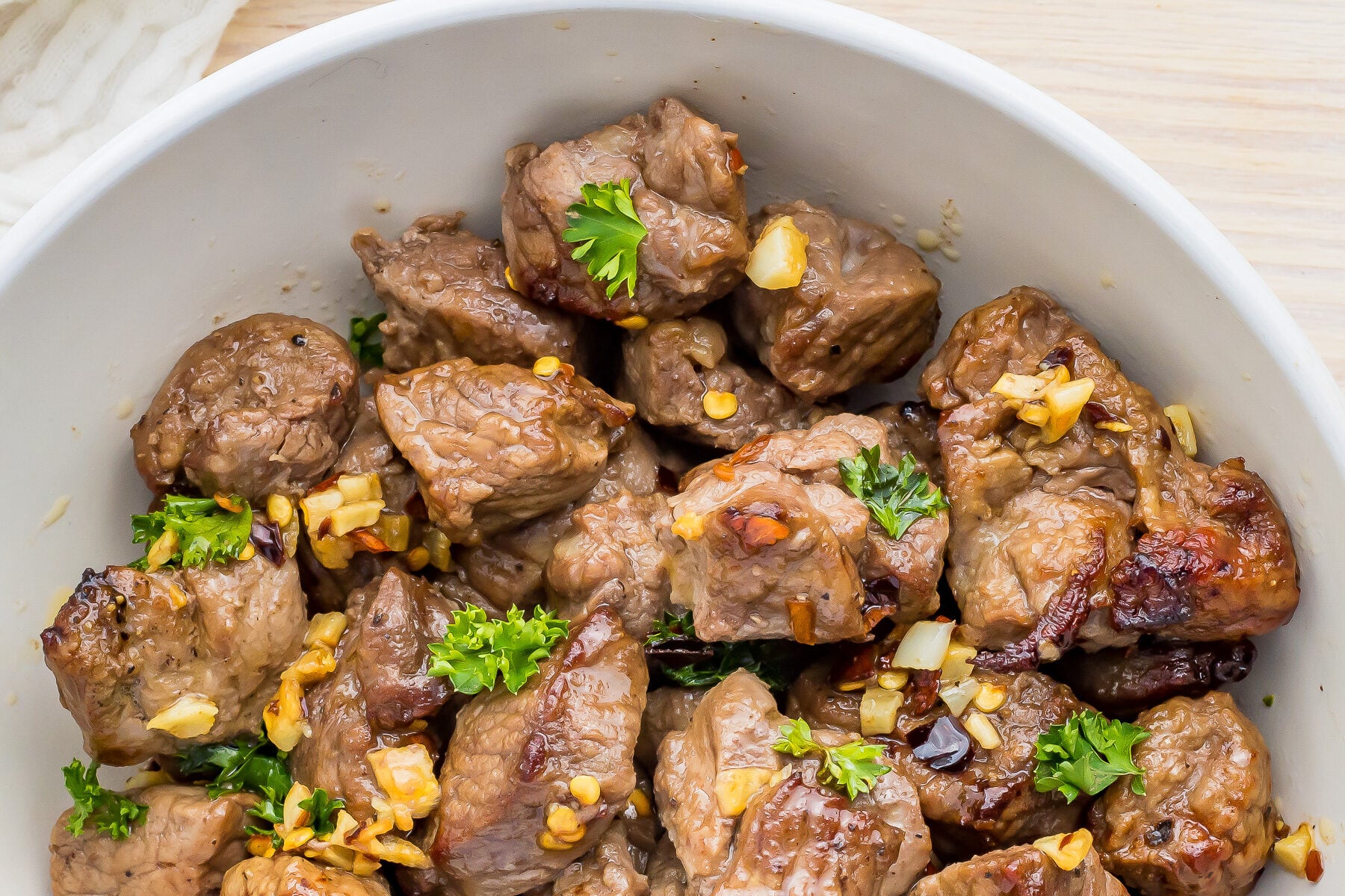Air Fryer steak bites served in a white bowl with meat and herbs.