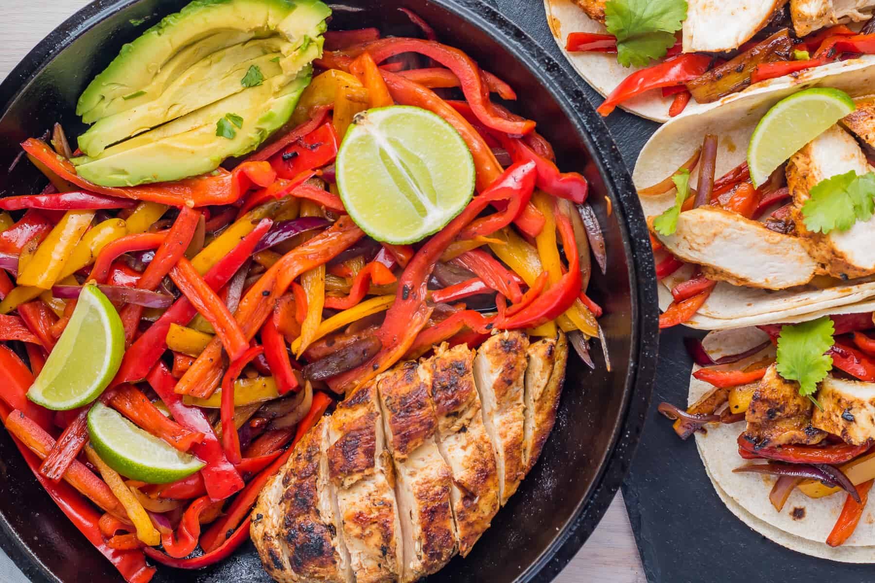 Authentic Mexican Chicken Fajitas with peppers and avocado cooked in a skillet.