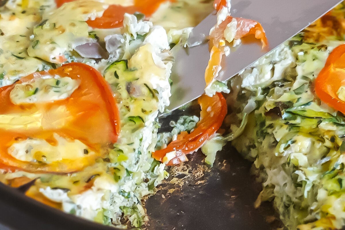 Knife lifting a slice of Greek Crustless Zucchini Quiche up (sfougato).