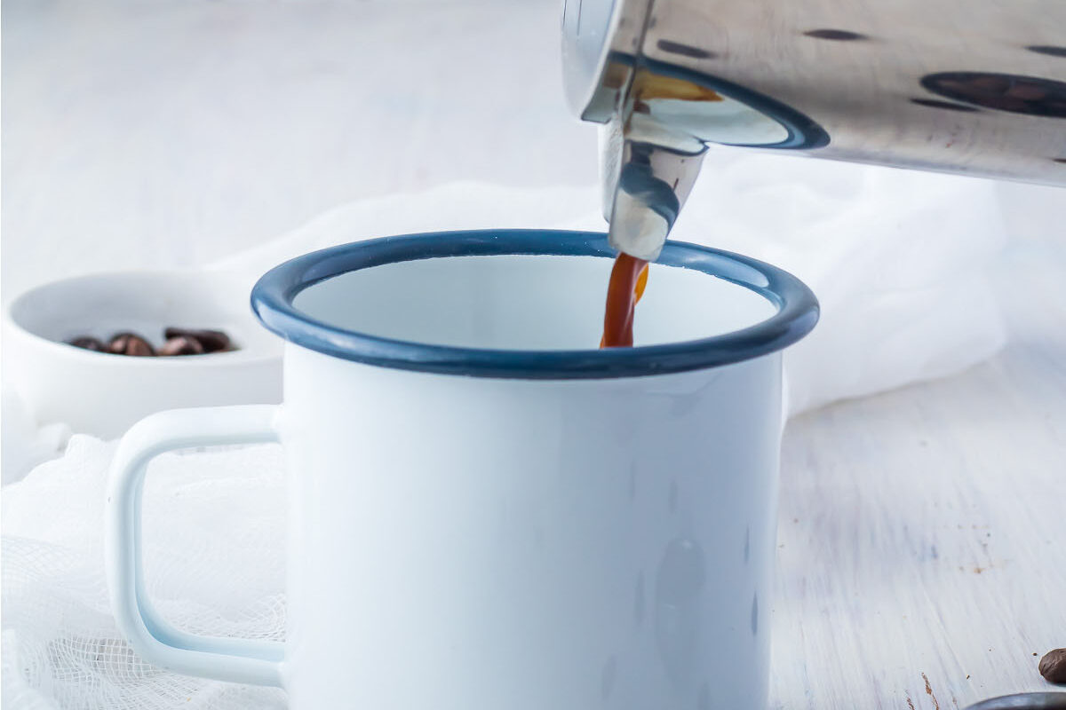 French press pouring espresso into a coffee cup.