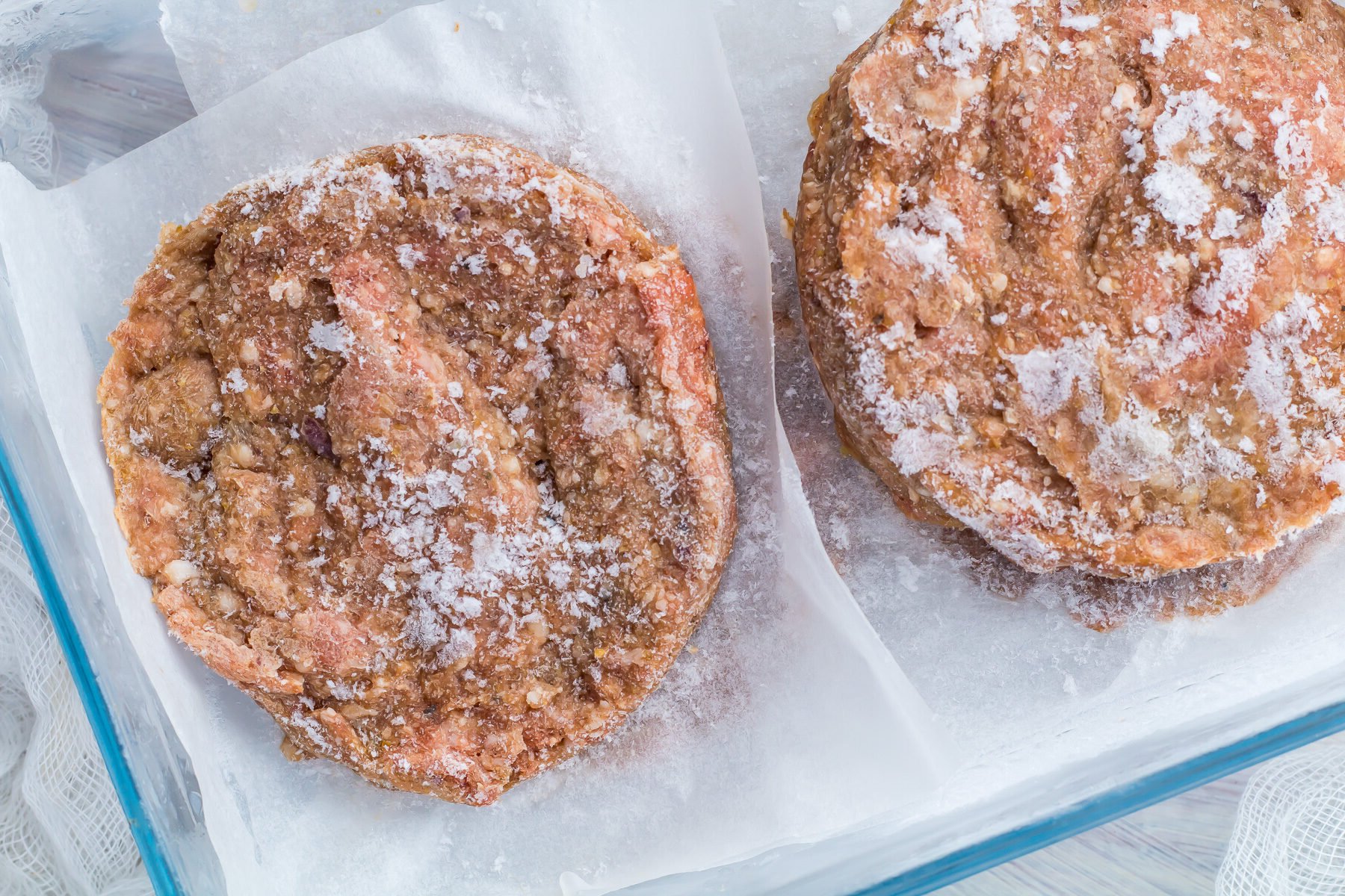 Stacked raw hamburger patties on parchment paper.