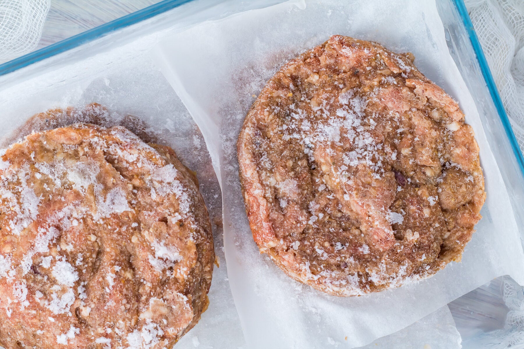 Stacked raw hamburger patties on parchment paper.