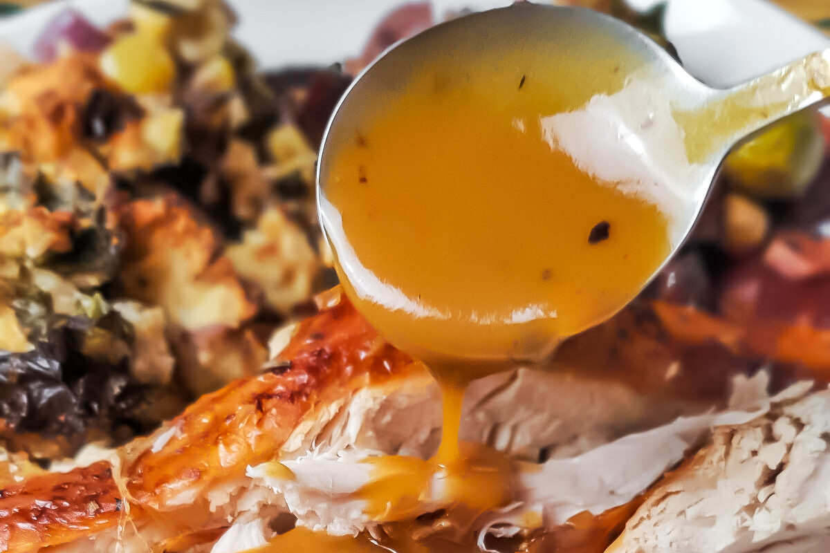 Gravy being spooned over turkey on a white plate with brussels sprouts and stuffing.