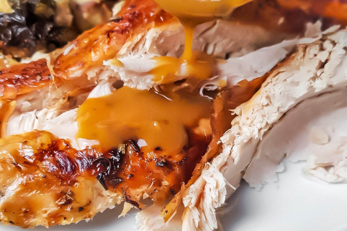Gravy being spooned over turkey on a white plate with brussels sprouts and stuffing.