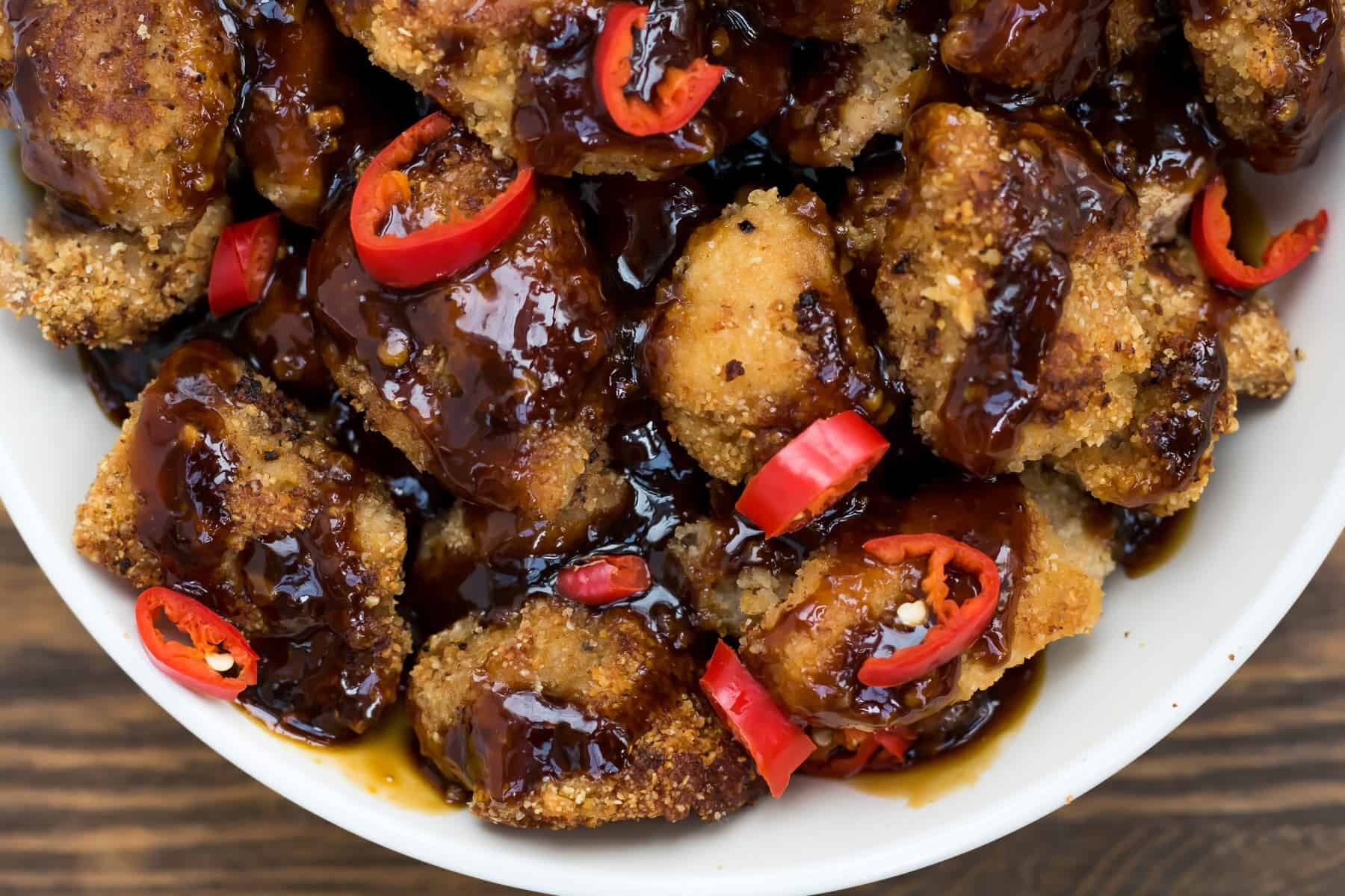 Paleo chicken wings in a white bowl with orange sauce and peppers.
