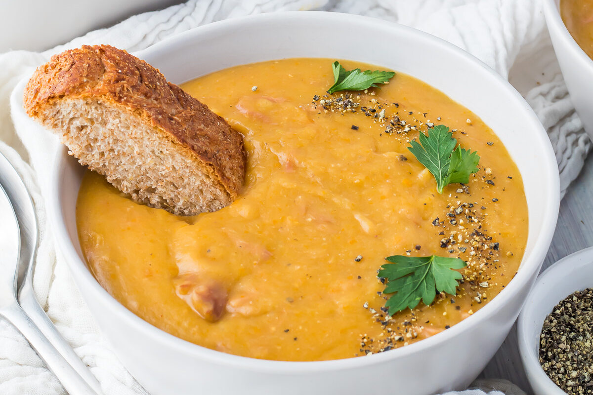 Three bowls of ham and lentil soup with bread on a table.