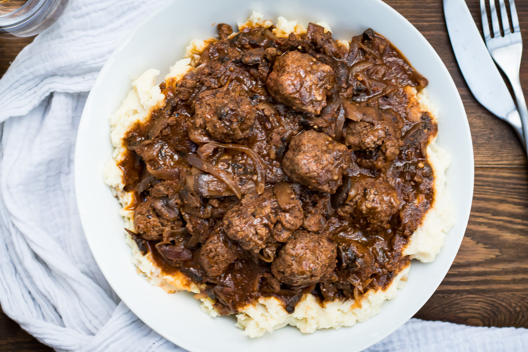 A bowl of meatballs with gravy and mashed potatoes.