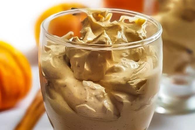 Two glasses with whipped cream and pumpkin spice pudding in them.